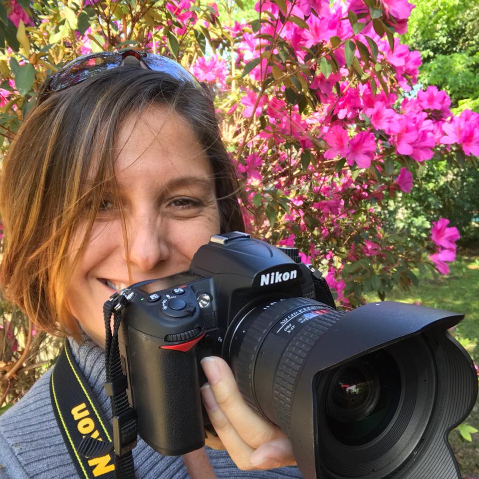 Kathleen Seide holding camera in front of flowers